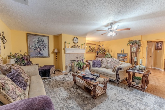 living area featuring wood finished floors, baseboards, a ceiling fan, a textured ceiling, and a tiled fireplace