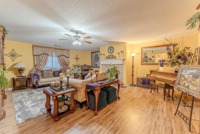 living area with a tiled fireplace, a textured ceiling, light wood-type flooring, and ceiling fan