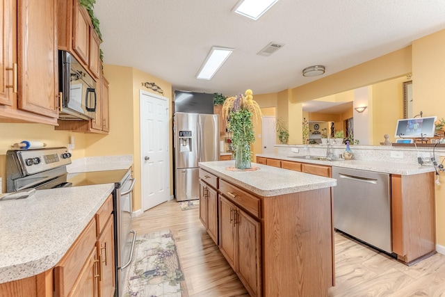 kitchen featuring a kitchen island, light wood-style flooring, a sink, stainless steel appliances, and light countertops