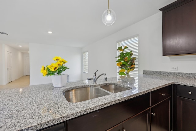 kitchen with light stone countertops, dark brown cabinetry, recessed lighting, hanging light fixtures, and a sink