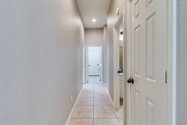 corridor with light tile patterned floors, baseboards, and a textured wall