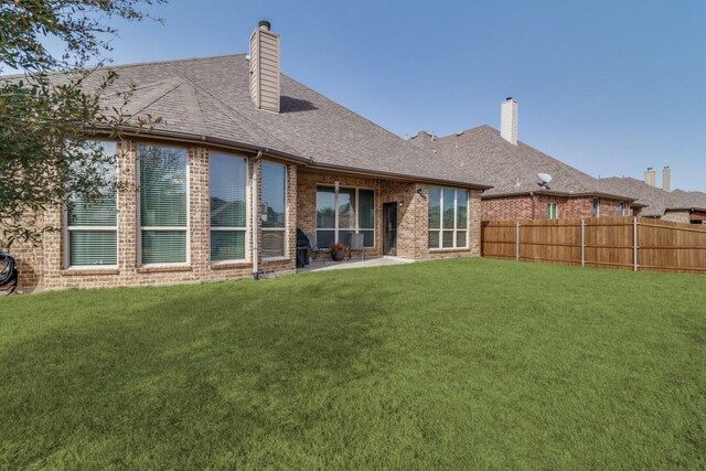 back of house with brick siding, fence, roof with shingles, a lawn, and a chimney