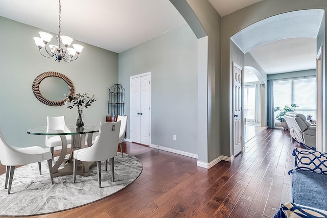 dining area with dark wood-type flooring, baseboards, arched walkways, and a chandelier