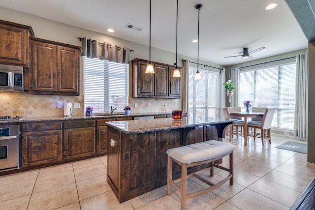 kitchen with a kitchen island, a breakfast bar, light tile patterned floors, dark stone countertops, and stainless steel appliances