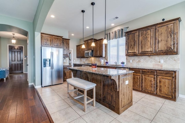 kitchen with visible vents, arched walkways, a sink, appliances with stainless steel finishes, and a center island