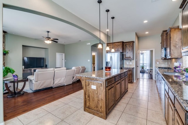 kitchen featuring light tile patterned floors, a ceiling fan, dark stone counters, arched walkways, and stainless steel appliances