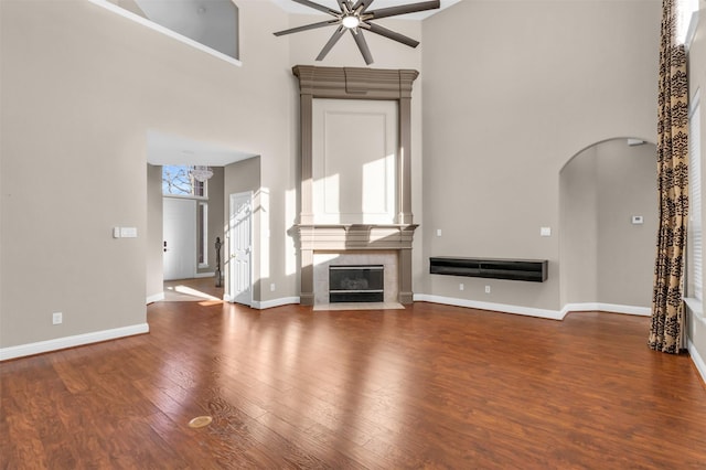 unfurnished living room with a tiled fireplace, a high ceiling, wood finished floors, and a ceiling fan