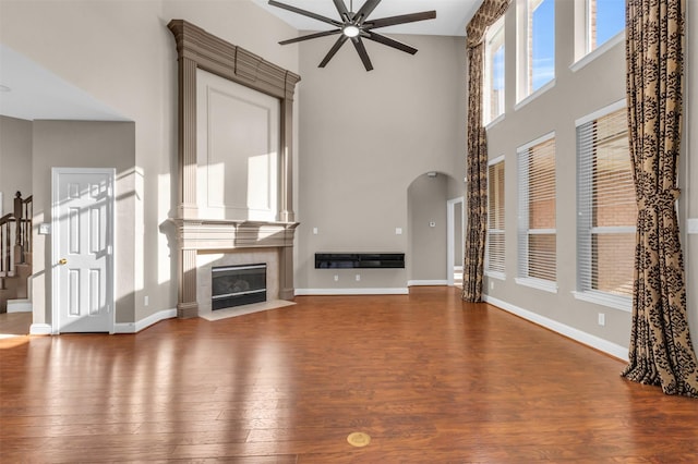 unfurnished living room featuring hardwood / wood-style flooring, a ceiling fan, arched walkways, and a premium fireplace