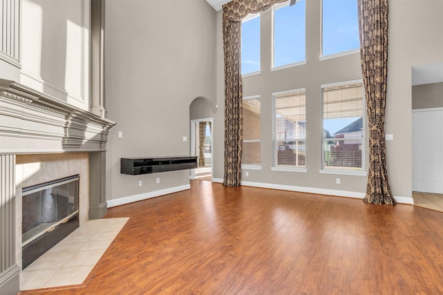 unfurnished living room featuring wood finished floors, arched walkways, a wealth of natural light, and a tile fireplace