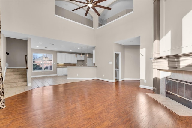 unfurnished living room with baseboards, light wood-style flooring, a fireplace, ceiling fan, and stairs