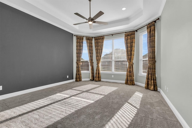 carpeted empty room featuring ceiling fan, crown molding, a raised ceiling, and baseboards