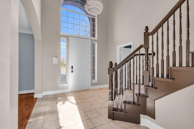 tiled entryway with a notable chandelier, stairway, a high ceiling, and baseboards