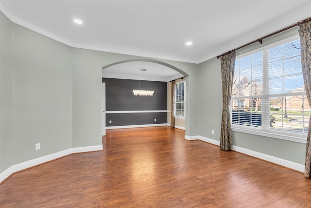 unfurnished room featuring arched walkways, plenty of natural light, ornamental molding, and wood finished floors