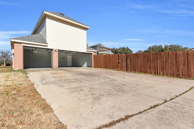 view of property exterior featuring fence, roof with shingles, concrete driveway, a garage, and brick siding