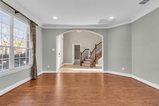 spare room featuring visible vents, arched walkways, light wood-style floors, and crown molding