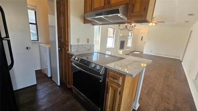 kitchen featuring dark wood-type flooring, range with electric cooktop, under cabinet range hood, brown cabinetry, and washer / dryer