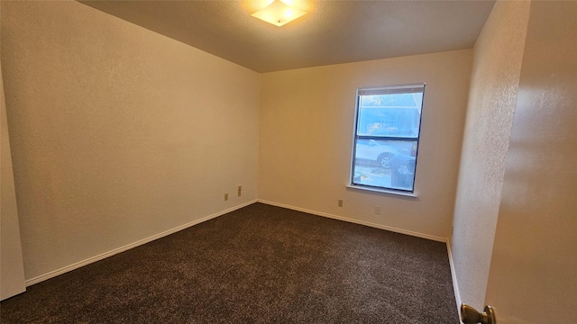 spare room with baseboards, dark carpet, and a textured wall