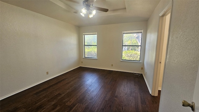 unfurnished bedroom featuring a ceiling fan, baseboards, dark wood finished floors, a raised ceiling, and a textured wall