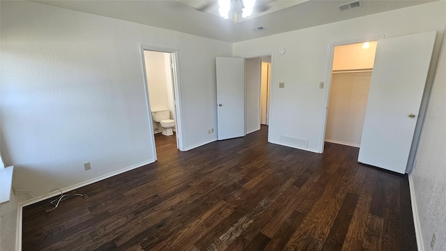 unfurnished bedroom with a spacious closet, visible vents, connected bathroom, dark wood-type flooring, and baseboards