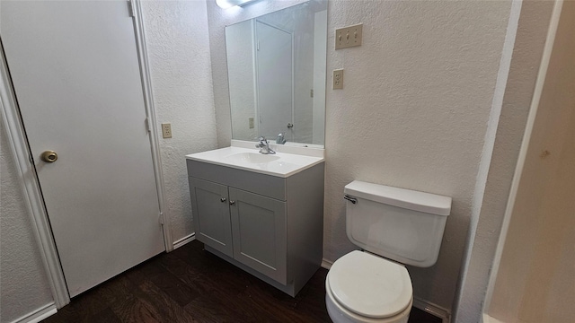 bathroom with toilet, vanity, a textured wall, and wood finished floors