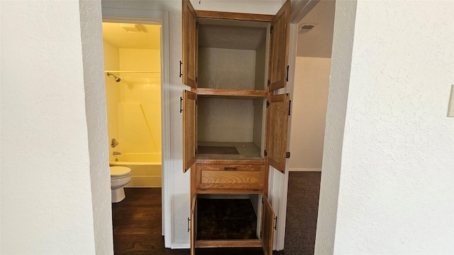 interior space featuring visible vents, toilet, wood finished floors, washtub / shower combination, and a textured wall