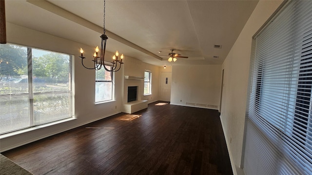 unfurnished living room featuring baseboards, dark wood finished floors, a fireplace with raised hearth, a raised ceiling, and ceiling fan with notable chandelier