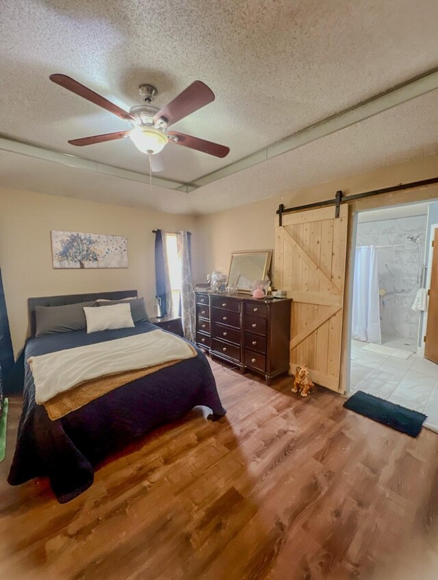 bedroom with a barn door, a textured ceiling, wood finished floors, and a ceiling fan