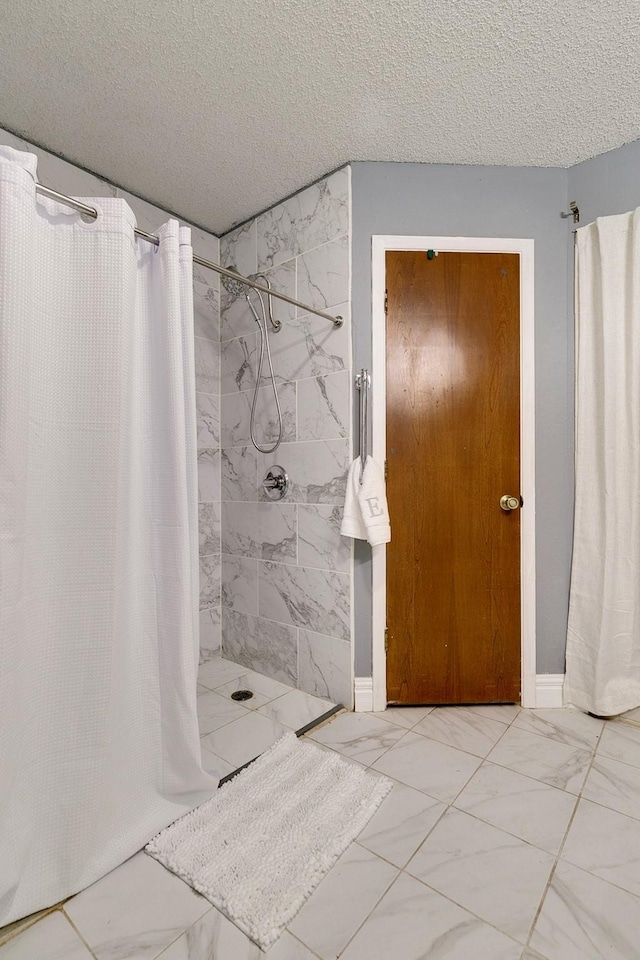 bathroom with baseboards, marble finish floor, a tile shower, and a textured ceiling