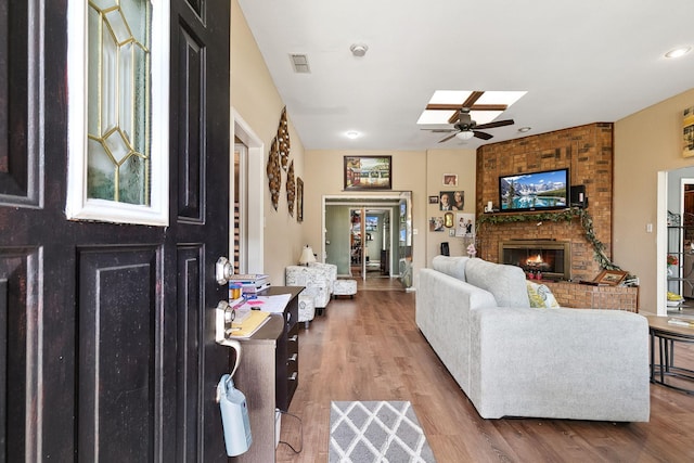 living area featuring visible vents, a fireplace, a skylight, wood finished floors, and a ceiling fan