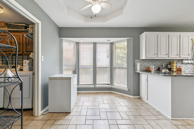 kitchen with tasteful backsplash, a tray ceiling, washer / dryer, dark stone countertops, and white cabinets