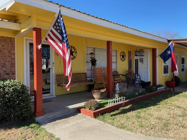 view of front of house featuring covered porch, brick siding, and metal roof