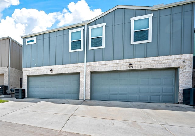 view of front facade featuring a garage, central AC unit, board and batten siding, and stone siding