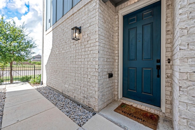 doorway to property featuring brick siding and fence