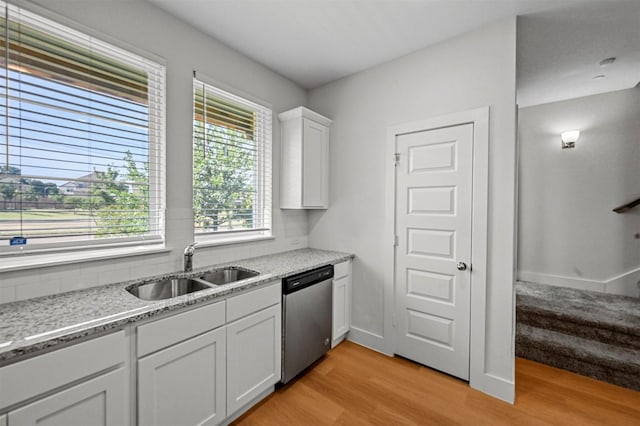 kitchen with light wood-type flooring, a sink, stainless steel dishwasher, white cabinetry, and light stone countertops