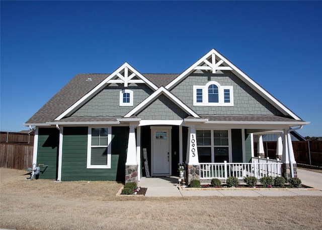 craftsman inspired home with covered porch, roof with shingles, and fence