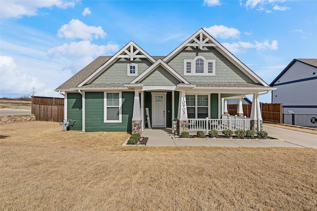 craftsman-style home featuring covered porch, a front lawn, and fence