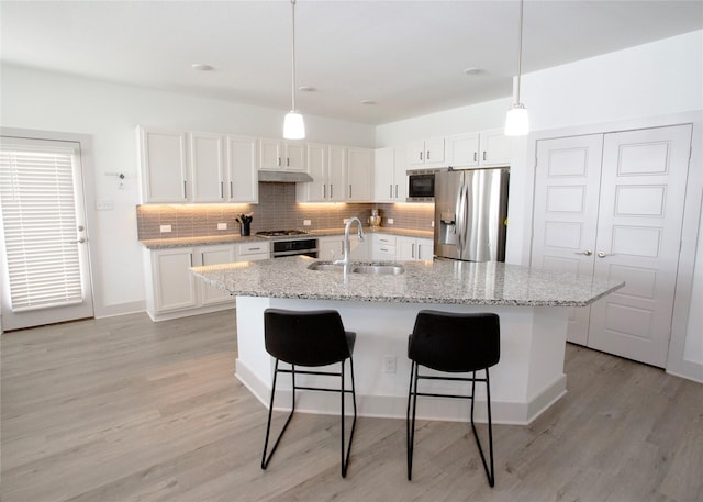 kitchen with a breakfast bar area, a sink, white cabinets, appliances with stainless steel finishes, and tasteful backsplash