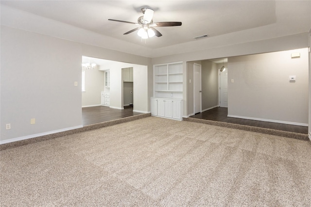 unfurnished room featuring visible vents, built in shelves, baseboards, carpet floors, and ceiling fan with notable chandelier