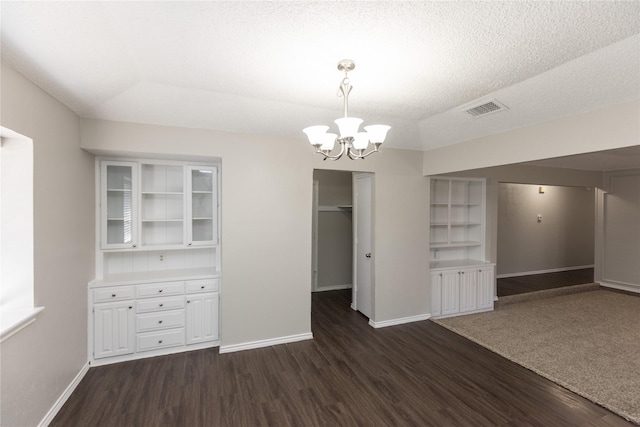 unfurnished dining area featuring dark wood finished floors, a notable chandelier, visible vents, and a textured ceiling