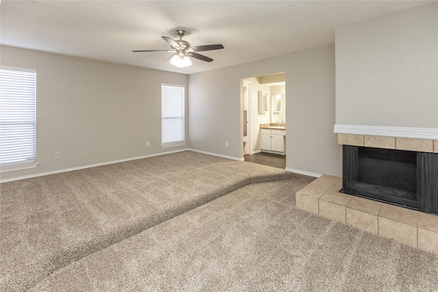 unfurnished living room with baseboards, carpet floors, ceiling fan, a tile fireplace, and a textured ceiling