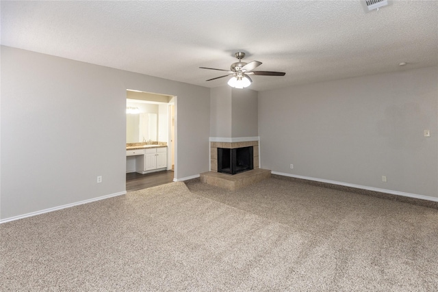 unfurnished living room featuring a tiled fireplace, a textured ceiling, carpet floors, baseboards, and ceiling fan