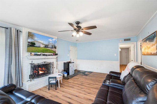 living area with visible vents, a brick fireplace, ceiling fan, and wood finished floors