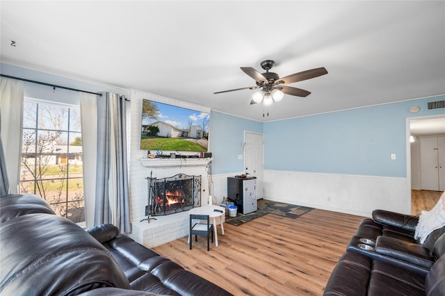 living area featuring a ceiling fan, a brick fireplace, and wood finished floors