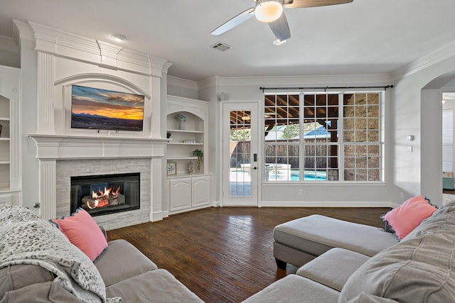 living area featuring built in features, wood finished floors, visible vents, a glass covered fireplace, and crown molding