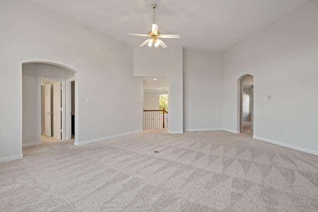 spare room with arched walkways, light colored carpet, baseboards, and a towering ceiling