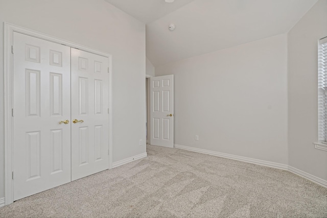 unfurnished bedroom featuring a closet, baseboards, lofted ceiling, and carpet floors