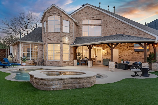 back of house at dusk with brick siding, a lawn, a patio, and roof with shingles