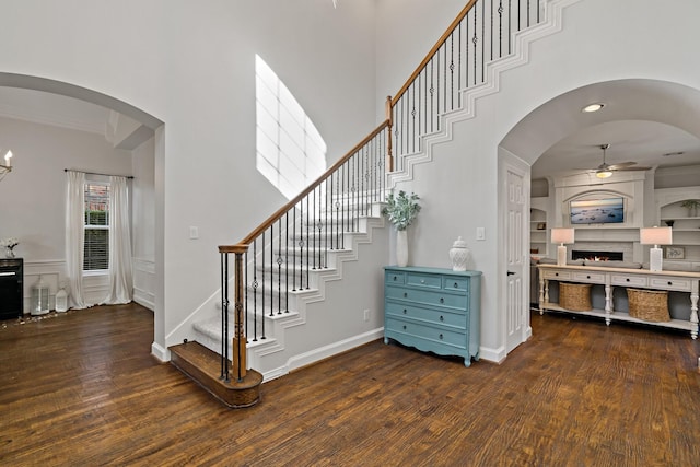 stairway with built in features, arched walkways, wood finished floors, and a ceiling fan