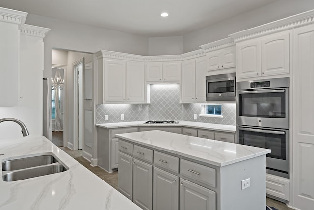 kitchen with light stone counters, decorative backsplash, appliances with stainless steel finishes, white cabinets, and a sink