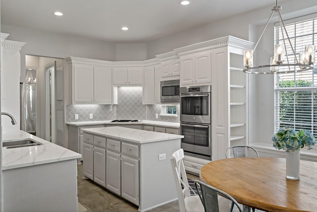 kitchen with stainless steel appliances, a sink, a notable chandelier, tasteful backsplash, and a center island